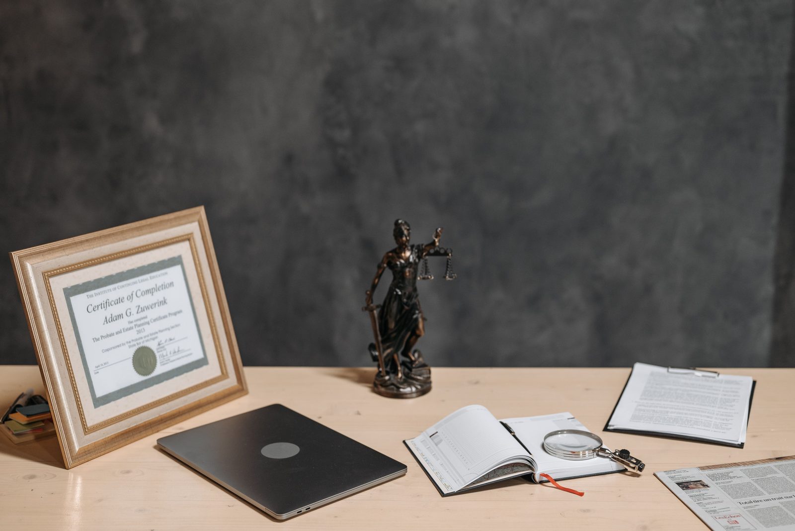 A framed certificate of completion beside a laptop and the scales of justice